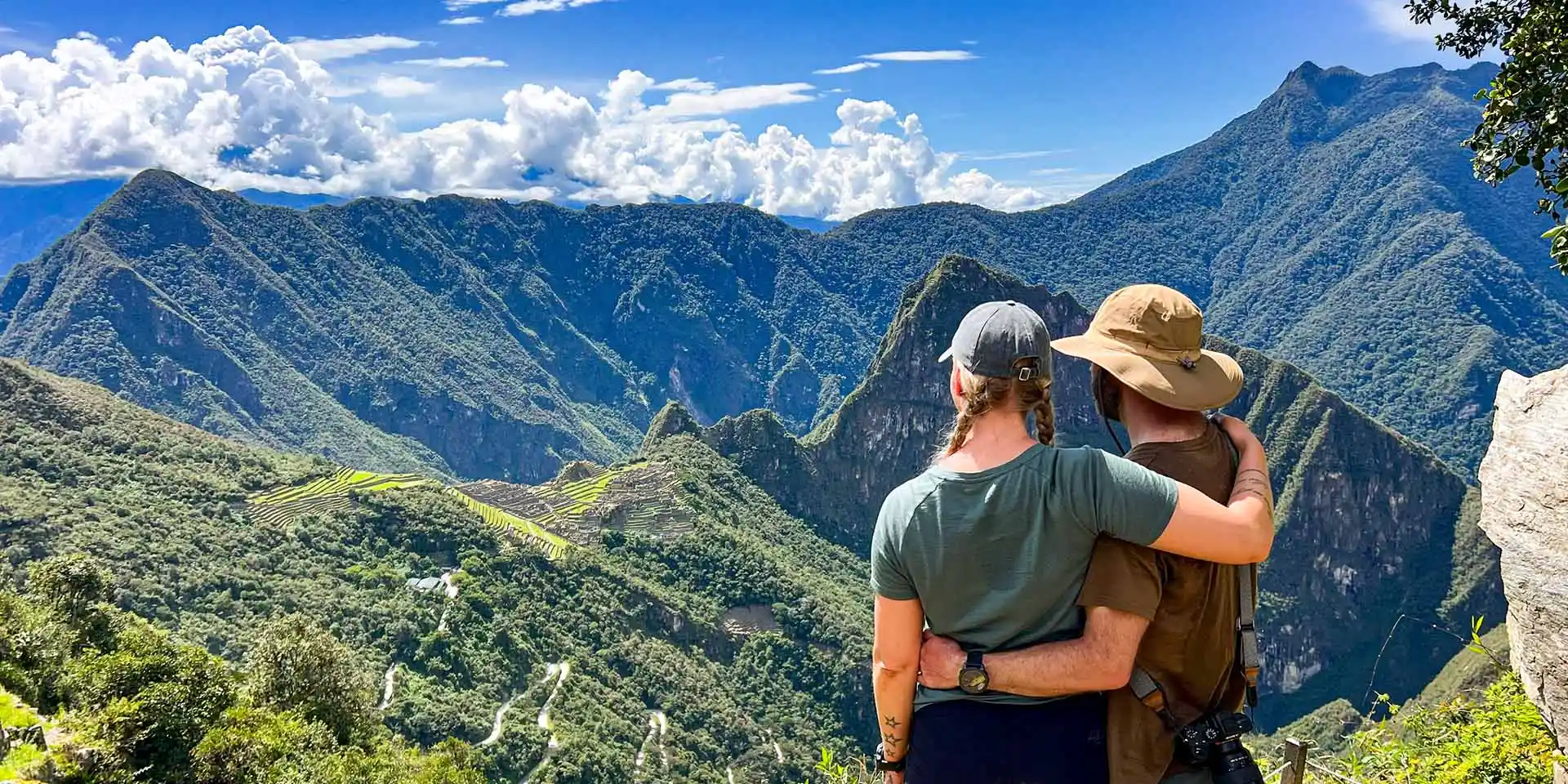 Breathtaking view of Machu Picchu from the Sun Gate A young couple hugging while looking at the Machu Picchu Inca citadel and Huayna Picchu mountain from a viewpoint.