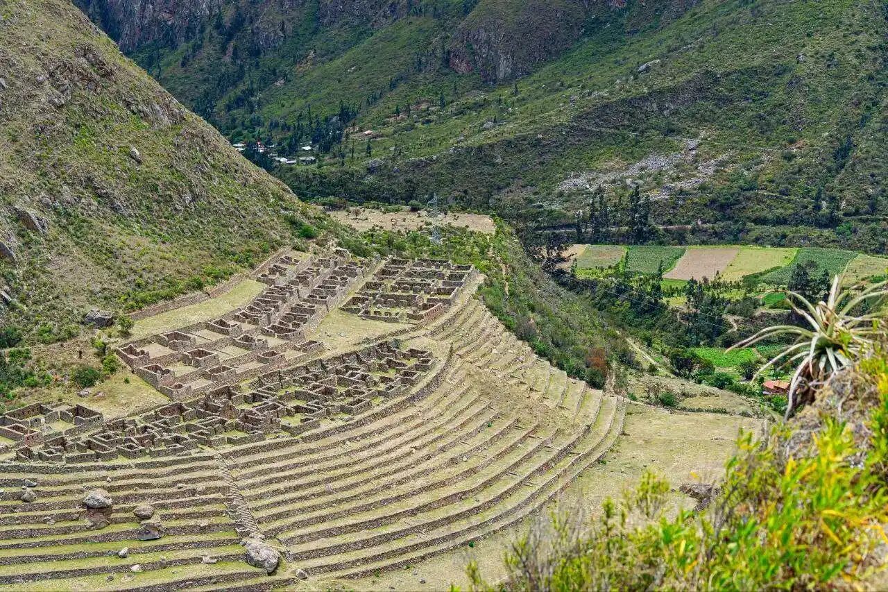 Walk the iconic classic Inca Trail to the Lost City of the Incas A stunning panoramic view of the original stone-paved Inca Trail winding its way up through a dramatic mountain pass. Dense Andean vegetation and other remote ruins are visible in the distance.