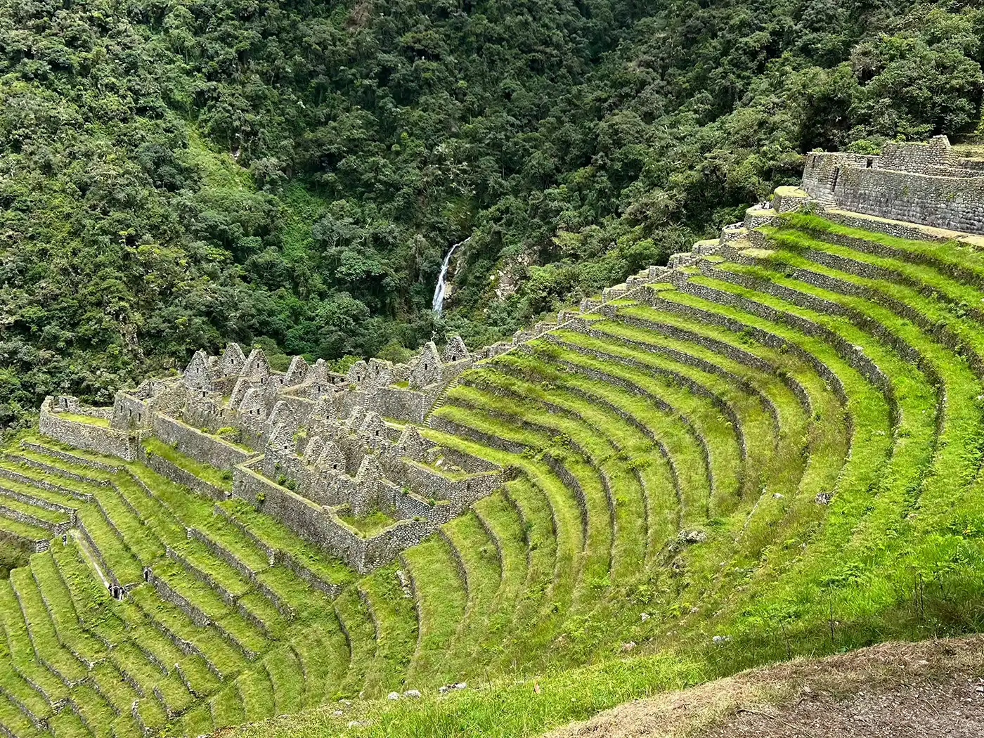 The breathtaking express route to Machu Picchu on the Inca Trail A dramatic high altitude Andean landscape with massive mountains and a winding river canyon. Part of the stone-paved Inca Trail is visible, leading towards Machu Picchu in the distance.