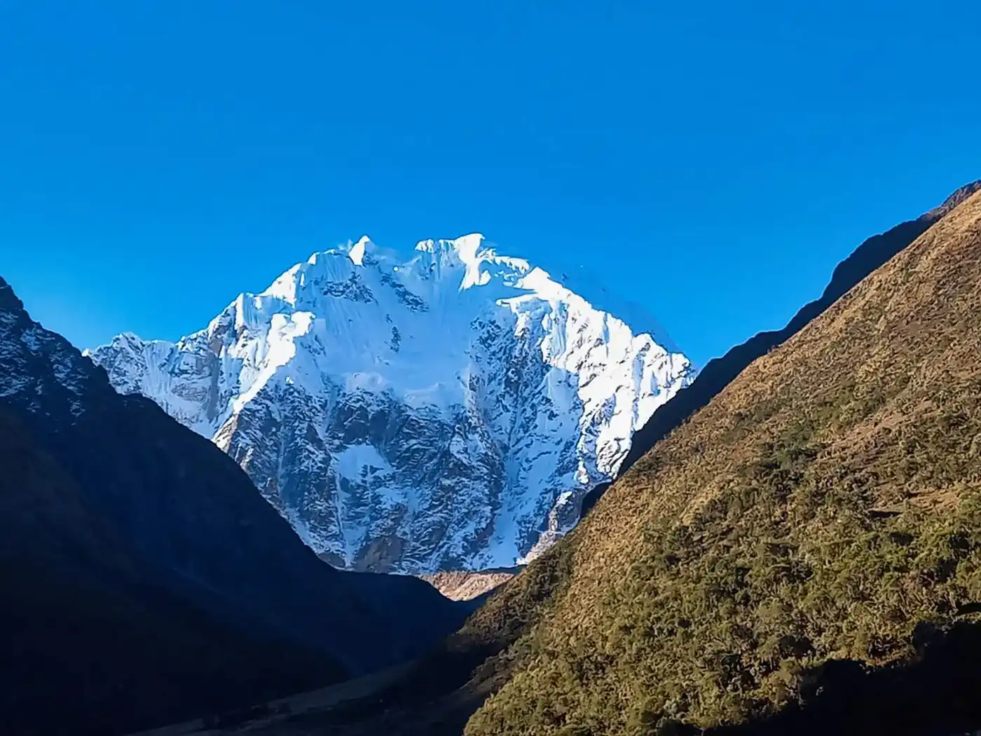 Conquering the majestic Salkantay, an epic adventure to Machu Picchu A sweeping panoramic landscape of the Salkantay trek. It features a massive snow-capped Salkantay nevado overlooking a dramatic high alpine valley with multiple glacier lakes and puna grasslands.