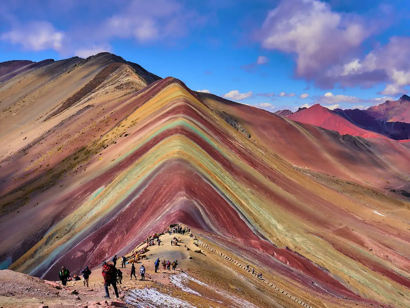 The breathtaking Vinicunca, a natural wonder of Peru A vibrant panoramic view of the Vinicunca Rainbow Mountain in Peru. A single person is walking along the colorful ridge trail, emphasizing the scale of the majestic Andean peaks.