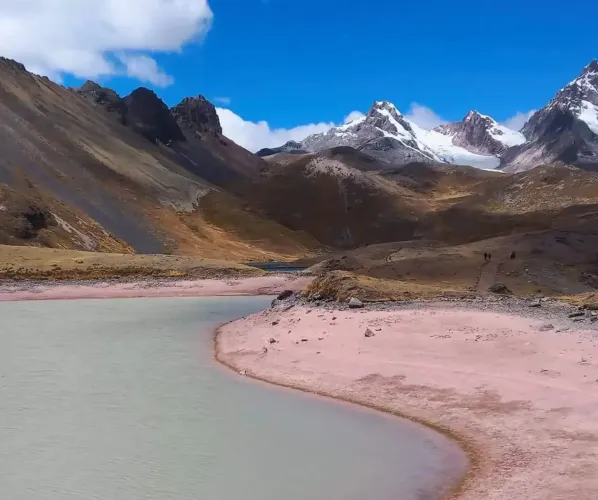 The stunning beauty of the high altitude Andes on the Ausangate route A breathtaking panoramic landscape of the Peruvian Andes during the Ausangate trek. It features a turquoise glacier lake, high altitude puna grasslands, and several snow-capped mountain ranges in the distance.