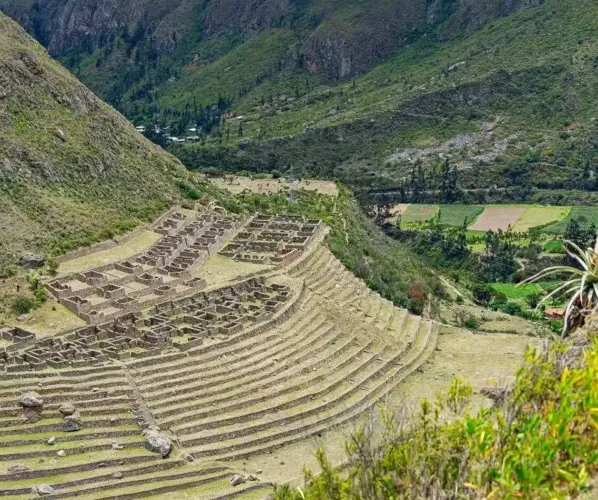 Walk the iconic classic Inca Trail to the Lost City of the Incas A stunning panoramic view of the original stone-paved Inca Trail winding its way up through a dramatic mountain pass. Dense Andean vegetation and other remote ruins are visible in the distance.