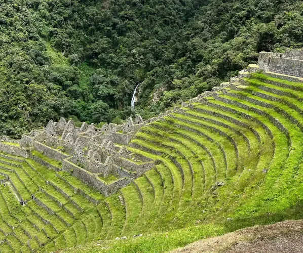 The breathtaking express route to Machu Picchu on the Inca Trail A dramatic high altitude Andean landscape with massive mountains and a winding river canyon. Part of the stone-paved Inca Trail is visible, leading towards Machu Picchu in the distance.