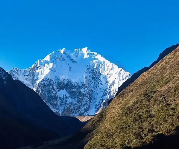 Conquering the majestic Salkantay, an epic adventure to Machu Picchu A sweeping panoramic landscape of the Salkantay trek. It features a massive snow-capped Salkantay nevado overlooking a dramatic high alpine valley with multiple glacier lakes and puna grasslands.