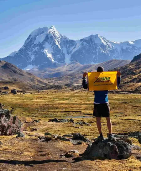 Conquering the mighty Ausangate, a true Andean experience A majestic close-up shot of a prominent snow-capped Andean peak during the Ausangate trek in Peru. A lone traveler is walking on a winding trail below, highlighting the mountain's grand scale.